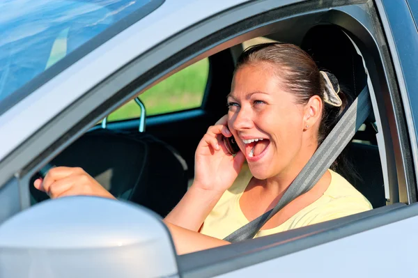 Beautiful girl behind the wheel with phone laughing — Stock Photo, Image