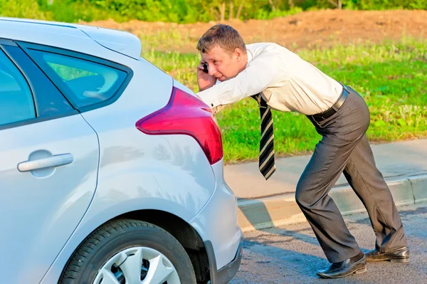 Empresário empurrando um carro e falando ao telefone — Fotografia de Stock