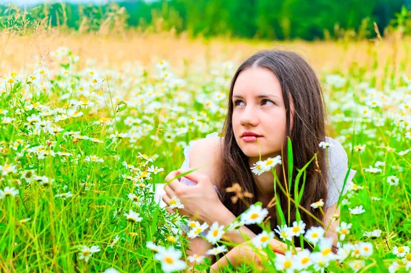 Bela mulher encontra-se em um campo verde com flores — Fotografia de Stock