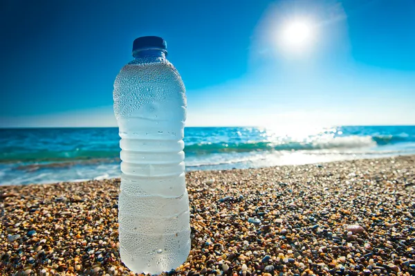 Garrafa de água fresca fria na praia de seixos — Fotografia de Stock