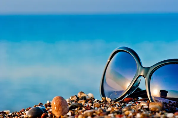 Sonnenbrille am Strand auf nassen Kieselsteinen liegend — Stockfoto