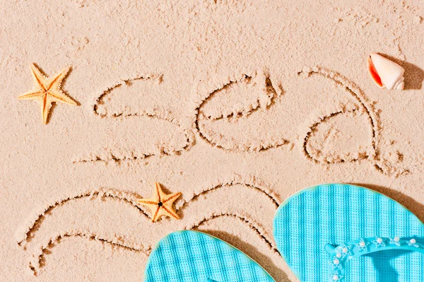 Zee inscriptie op de natte zand en het strand accessoires — Stockfoto