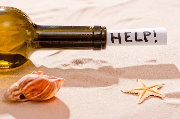 Bottle requesting assistance and seashells on the beach — Stock Photo, Image