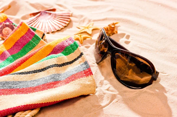 Striped beach towel and sunglasses on a sandy beach — Stock Photo, Image