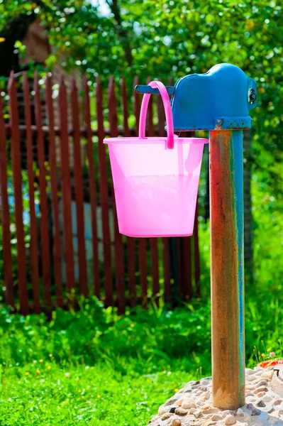 Pinkfarbener Plastikeimer und ländlicher Brunnen — Stockfoto