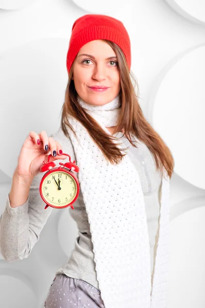 Girl in scarf and hat shows the time on the alarm clock — Stock Photo, Image