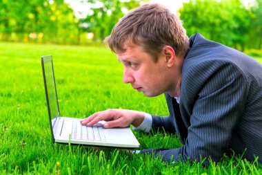 çim üzerinde yalan bir dizüstü bilgisayar ile çalışan adam