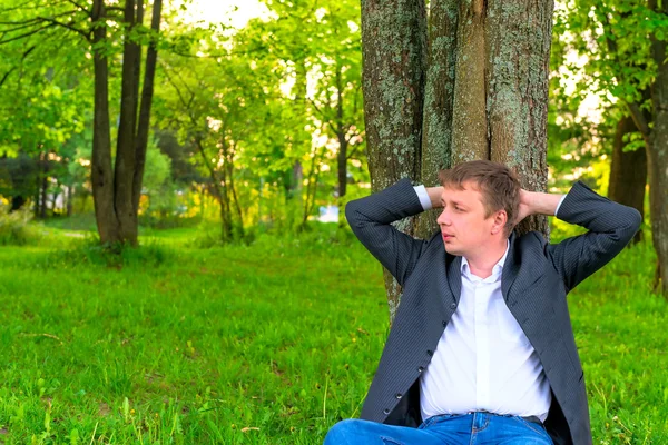 Young man resting near a tall tree — Stock Photo, Image