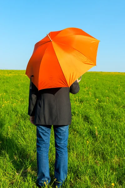 People under an orange umbrella in a field waiting for rain — Stock Photo, Image