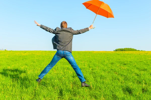 Homme d'affaires avec parapluie sautant dans un champ — Photo