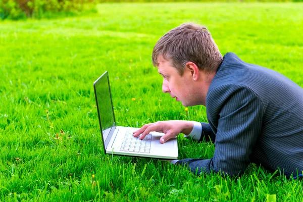 Homem de negócios encantador encontra-se na grama com laptop — Fotografia de Stock