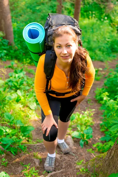 Kvinna med en ryggsäck uppför backen i skogen — Stockfoto