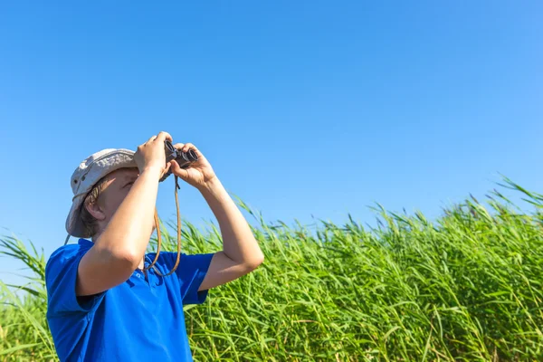 Man looks for through the reeds with binoculars — Stock Photo, Image