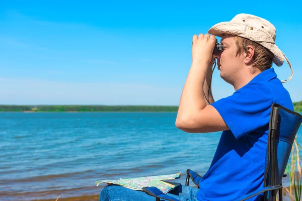 Young man near the lake looking through binoculars — Stock Photo, Image