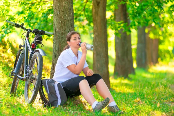 Jonge vrouw met fles water rusten in de buurt van een boom — Stockfoto