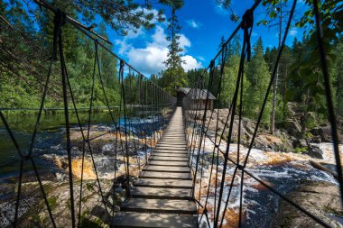 Suspension bridge and wooden house on Ruskeala waterfalls in Karelia, Russia clipart