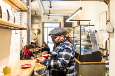 Ekose gömlekli ve yün şapkalı sakallı bir adam kahve dükkanında espresso tadıyor.