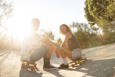 Genç kaykaycı çift, gün batımında nehir kanalındaki kaykay seansından sonra telefonlarıyla selfie çekerken gülümsüyor..