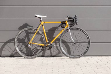 Gri bir duvara dizilmiş klasik sarı Fixie yol bisikleti