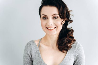 Güzel, genç bir kadın gülümsüyor, kameraya bakıyor. Gri duvarda yalnız poz veren kız.