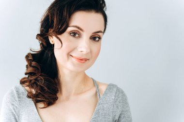 Gri arka planda gülümseyen tatlı, gülümseyen bir esmer. Boş duvar arka planında izole edilmiş sevimli genç kadın, kopyalama alanı.