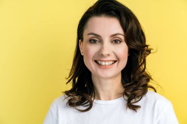 Kapatın. Mutlu, neşeli esmer, sarı bir duvarın arkasında duruyor. Kopya arkaplanındaki izole kadın.