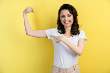 Sarı arka planda izole edilmiş güçlü kol kaslarını gösteren güzel görünümlü, çekici bir kızın yakın plan portresi. Boş bir duvarın arkasında poz veren kız.