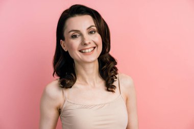 Gülümseyen, pembe duvar arkasında poz veren genç bir kadın. Çekici esmer, pembe arka planda soyutlanmış..