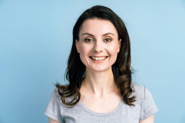 Gülümseyen, mavi duvar arkasında poz veren genç bir kadın. Çekici esmer, mavi bir arka planda izole edilmiş..