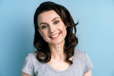 Kapatın. Mutlu, neşeli esmer, mavi bir duvarın arkasında duruyor. Kopya arkaplanındaki izole kadın.