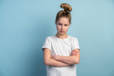 Genç kız kollarını göğsünde kavuşturdu ve mavi arka plandaki kameraya baktı. Kız öfkeyle fotokopi odasında izole edilmiş gibi görünüyor..