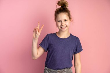 Gülümseyen genç kız zaferin ve barışın bir göstergesi. Pembe arka planda poz veren güzel küçük kız..