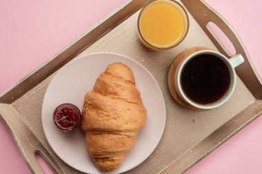 Kahveyle kahvaltı, kruvasan, pembe arka planda tahta tepside meyve suyu. Yatakta kahvaltı. Kahvaltı konsepti.