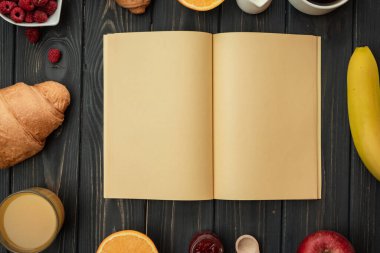 Ahşap zemin üzerinde boş bir kağıt parçası, yazı yazmak için yer. Koyu bir arka planda lezzetli bir kahvaltı, kruvasan, kahve, meyve suyu, ahududu.