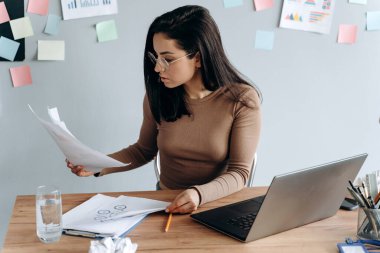 Dizüstü bilgisayarda çalışan güzel bir kız. Önemli belgeleri bölüyor. Genç bir kadın, renkli çıkartmalarla yapıştırılmış gri arka plandaki her şeyi dikkatle inceliyor..
