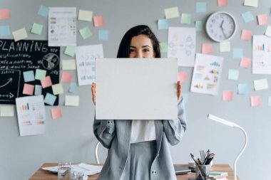 Esmer, beyaz, gri arka planda boş bir kağıt parçası tutan iş kadını, çıkartmalar. Reklam için yer, kopyalama alanı.