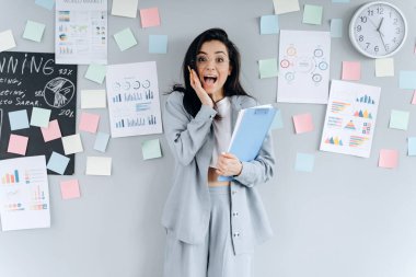 Gri arka plandaki belgelerle etiketleri karıştırmış bir iş kadını. Gözlüklü güzel esmer işi için endişeleniyor..