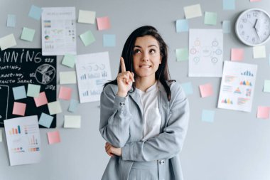 Utangaç, genç kız parmağını kaldırdı. Başka tarafa bakıyor ve başparmağını kaldırıyor. Gri arkaplanda izole