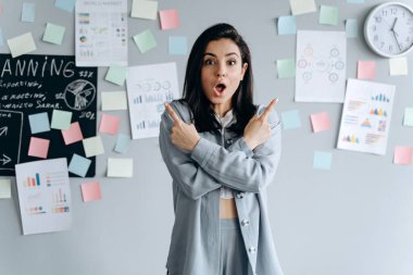 Gri iş geçmişi olan güzel bir iş kızı işaret parmaklarını kaldırmış, kollarını kavuşturmuş. Ofisteki hoş genç bayan..