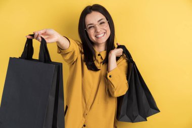 Gözlüklü, turuncu stüdyo arka planında alışveriş torbaları taşıyan şık bir kadın. Fotokopi alanındaki genç kadın