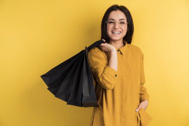 Gülümseyen esmer, turuncu arka planda alışveriş yaparken seviniyor. Elinde torbalar tutuyor..