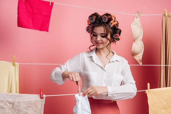 Çekici, çalışkan, neşeli ev kadınının portresi. Çamaşır ipine ıslak giysiler asıyor. Pembe arka planda izole edilmiş. Ev temizliği kavramı.
