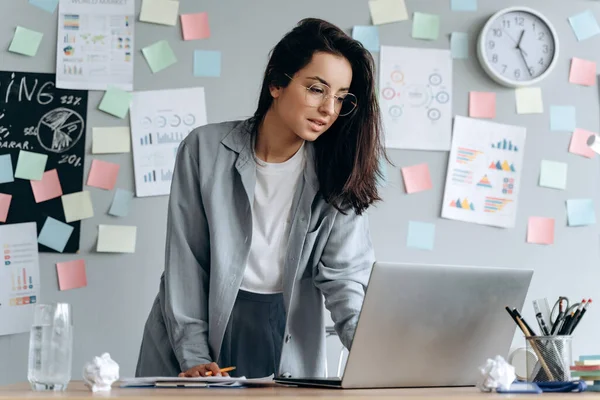 Ofisteki odaklanmış genç bayan. Dizüstü bilgisayarda çalışan güzel kız..