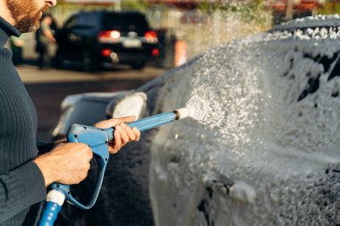 Açık hava oto yıkama servisinde yüksek basınçlı spreyle siyah arabanın yatay görüntüsünü kapat. Temiz araba konsepti 