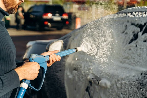 Açık hava oto yıkama servisinde yüksek basınçlı spreyle siyah arabanın yatay görüntüsünü kapat. Temiz araba konsepti 
