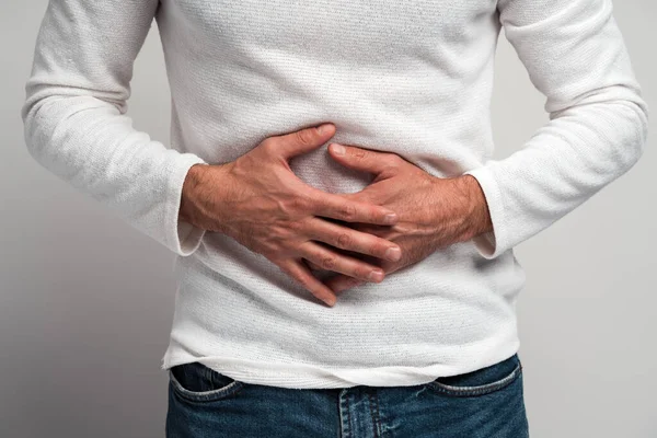 Karın üstü el ele tutuşan, şiddetli ağrı çeken hazımsızlık çeken, mide bulantısı çeken, duodenal ülser olan adamın yakın görüntüsü. Beyaz arka planda izole edilmiş kapalı stüdyo görüntüleri 