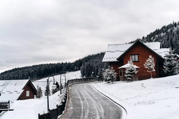 Karlı dağlarda ahşap evle muhteşem kış manzarası. Noel tatili kavramı. Köyün yakınındaki ıssız yolda. 
