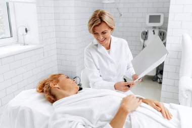 Şuna bir bak. Kafkasyalı kıdemli doktorun hasta kadın dosyasına müşteri anlaşmasıyla birlikte gösterdiği belden yukarı portre görüntüsü.