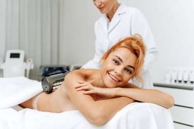 Masaya uzanmış gülümseyen kadın yüzüne ve yenilenen tedaviye yakın durun. Kozmetik uzmanı sırtında özel ekipman taşıyor. Güzellik konsepti 