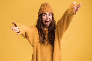 Kaygısız duygular. Enerjik, neşeli, tapılası kız ellerini kaldırıyor ve mutluluktan çığlık atıyor, zafere seviniyor, şakaya gülüyor. Sarı arka planda kapalı stüdyo çekimleri 